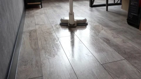 Modern beige vacuum cleaner operating on grey tile floor surfaces Stock Footage 345023857