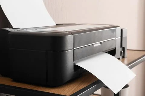Modern black inkjet printer with blank paper sheets on wooden desk, office te Stock Photos
