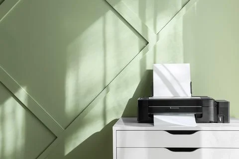 Modern black inkjet printer with blank paper on white desk against green wall Stockfoto's