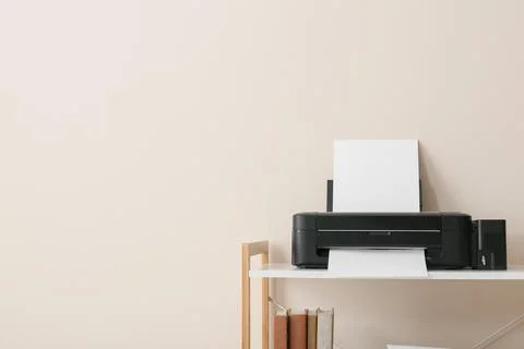 Modern black inkjet printer with blank paper on white shelf, home office tech Stock Photos