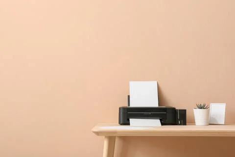 Modern black inkjet printer with blank paper on wooden desk against peach wal Stock Photos