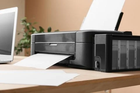 Modern black inkjet printer with paper on wooden desk, home office technology Stock Photos