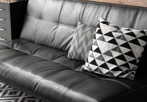 Modern black leather sofa with geometric patterned throw pillows and white st Stock Photos