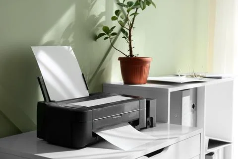 Modern black printer with blank paper on a white desk in a home office settin Stock Photos
