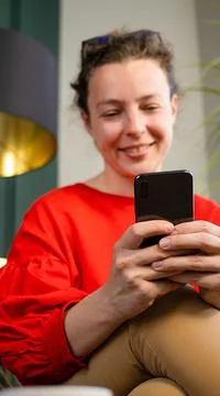 Modern black smartphone close up in woman hands, sitting indoors, wearing red Stock Photos