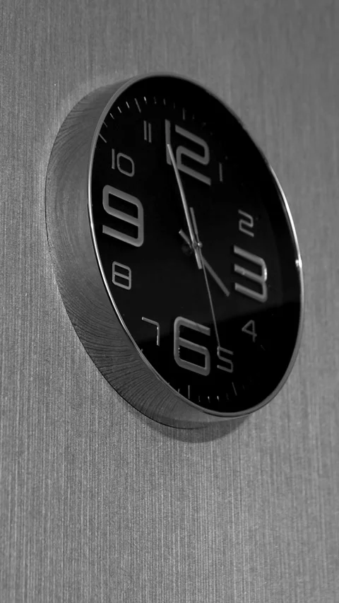 Modern black wall clock mounted on a textured metallic wall in close-up. Ve.. 库存影片 342036087