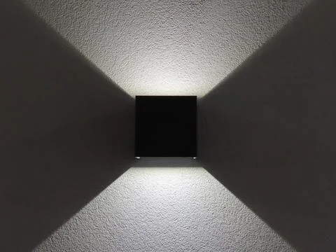 Modern black wall lamp casting symmetrical light patterns on a white textur.. Stock Photos