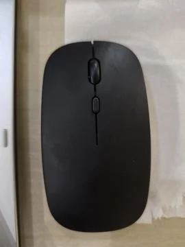 Modern Black Wireless Computer Mouse Resting on a Clean Wooden Desk Surface Foto stock