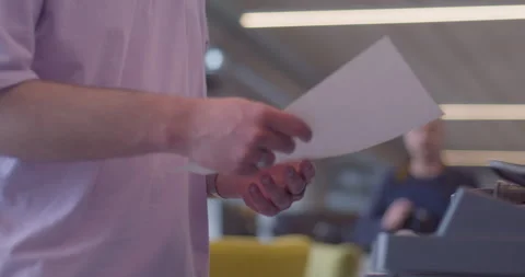 A modern, blond-haired man efficiently operates a high-tech paper printer in a Stock Footage 254527237