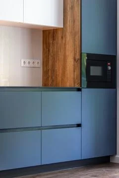Modern blue kitchen with built-in microwave. Wood accents add contrast. Stock Photos