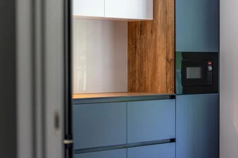 Modern blue kitchen seen through doorway. Built-in microwave and wood details Stock Photos