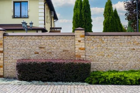 Modern brick pattern of light stone fence wall with posts in front of a resid Stock Photos