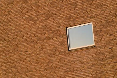 Modern brick wall with a single square window reflecting the sky on a sunny d Stock Photos