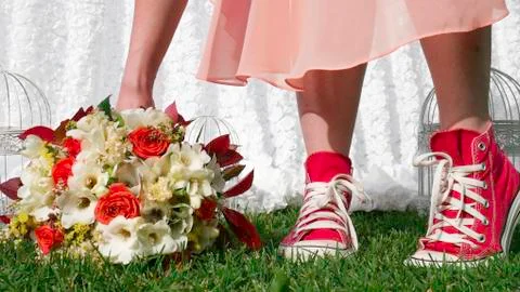 Modern bride in red sneakers taking a bouquet from the grass - close up. Stock Photos