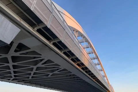 Modern bridge underside with geometric beams under golden light against blue sky Stockfoto's