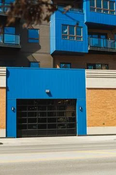 A modern building with a blue facade features a large garage door facing a bu 스톡 사진