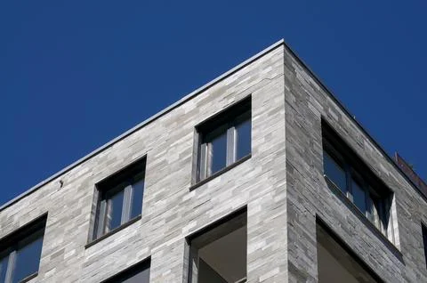 Modern building facade with grey stone cladding under blue sky Stock Photos