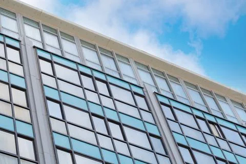Modern building facade with rectangular windows that reflect the blue sky and Stock Photos