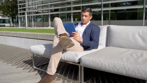 Modern businessman using tablet on outside sofa in business park 4K Stock Footage 96055961