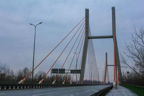 Modern cable-stayed bridge spans a quiet highway in overcast weather Stock Photos