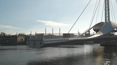 Modern cable-stayed pedestrian bridge spanning a tranquil river under blue sky Stock Footage 315737830