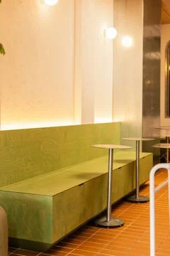 In a modern cafe, two small round tables stand beside a long green bench. The Stock Photos