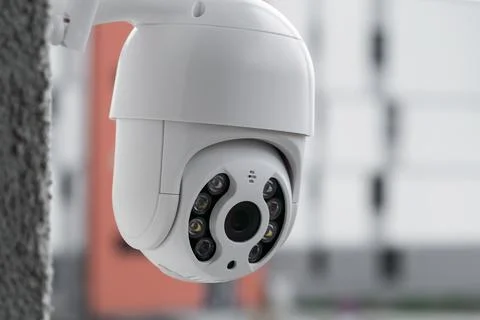 Modern CCTV camera on a wall with a blurred multi-storey building on the Stock Photos