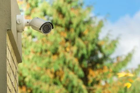 Modern CCTV security camera on building wall, foliage background Stock Photos