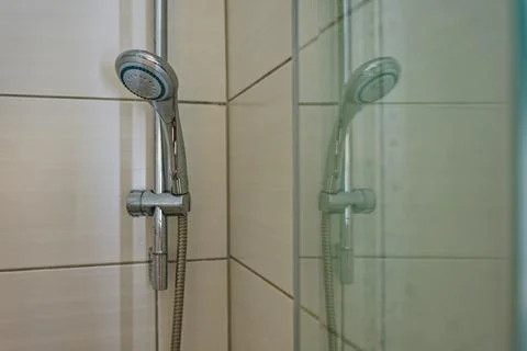 Modern chrome handheld showerhead mounted on tiled bathroom wall with glass.. Stock Photos