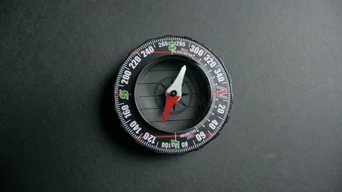 A modern compass lying on a black desk with a red arrow that shows the direction Stock Footage 139805145