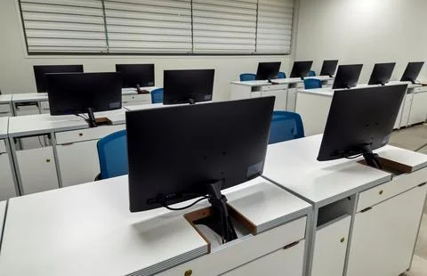 Modern computer classroom with rows of monitors and white desks Stock Photos