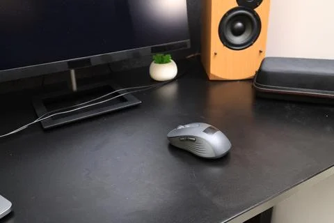 Modern computer mouse and speaker on a clean black desk surface Stock Photos