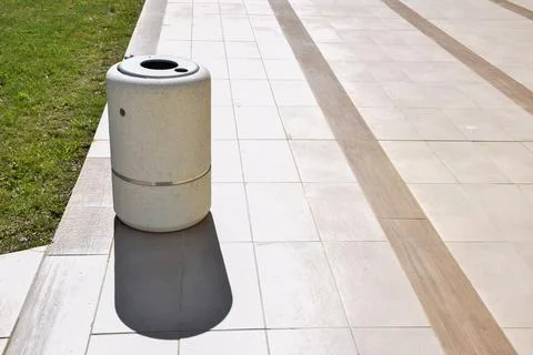 Modern cylindrical trash bin on tiled pavement in outdoor setting Stock Photos