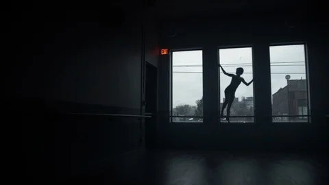 Modern dancer on window sill dancing in large dark moody dance studio 스톡 동영상 104275660