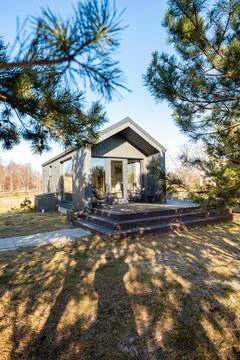 Modern dark cabin with steep gable roof on raised deck among pines Stock Photos