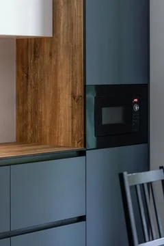 Modern dark kitchen with built-in microwave. Warm wood adds contrast. Stock Photos
