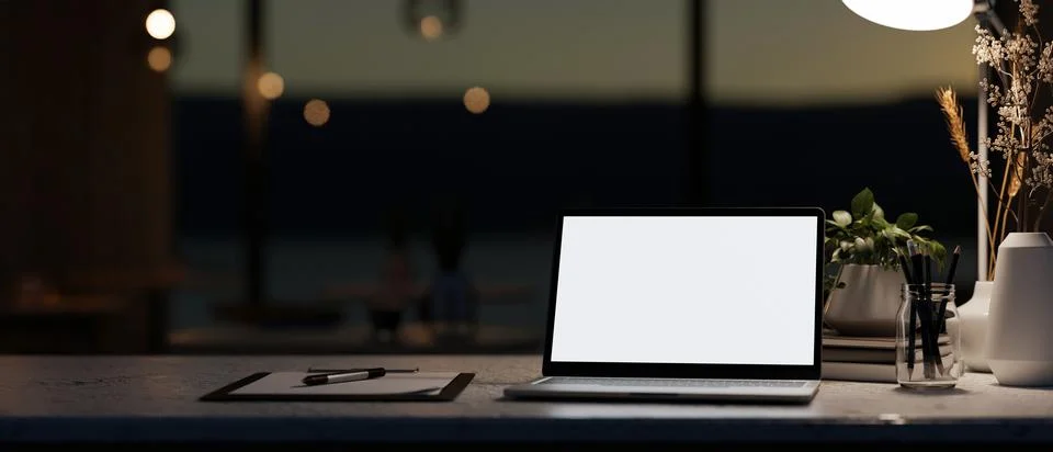 A modern dark office at night featuring a white-screen laptop computer mock.. Fotos de archivo