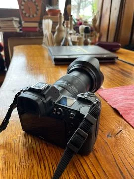 Modern digital camera in black with a large lens on a wooden table. Stock Photos