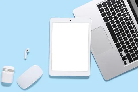 Modern digital workspace with laptop tablet wireless earbuds and mouse on blu Stock Photos