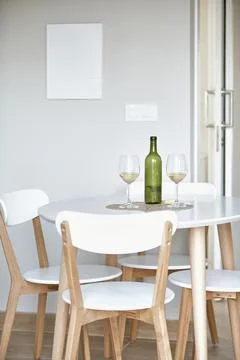 Modern dining room with white table, wooden chairs, wine bottle, and two gl.. Stock Photos