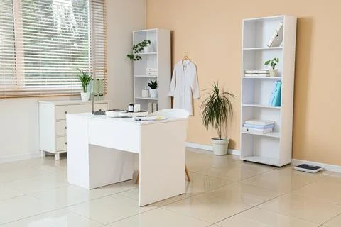 Modern doctors office interior with a white desk, laptop, medical coat, and b Stock Photos