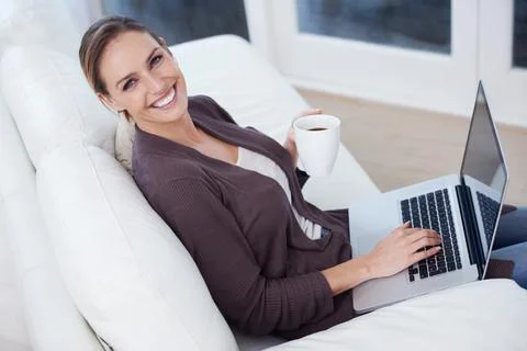 Modern domestic life. A young woman sitting in front of her laptop holding a mug Stock Photos