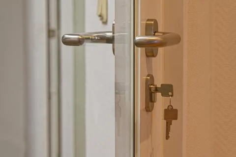 Modern door handle with key inserted in lock on white interior door Stock Photos