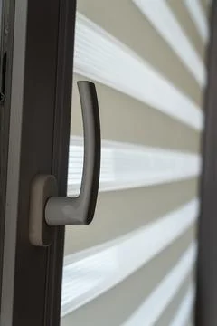 Modern door handle on a window showcasing layered white roller blinds, creating Stock Photos