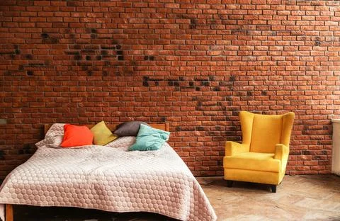 Modern double bed and yellow armchair stand against brick wall background Stock Photos
