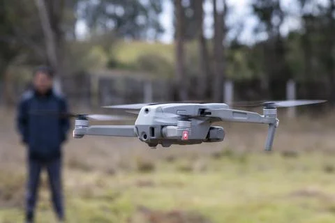 Modern drone in flight with blurred operator in background Stock Photos