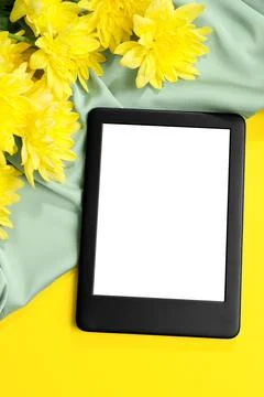 Modern e-book reader and flowers on yellow background, flat lay Stock Photos
