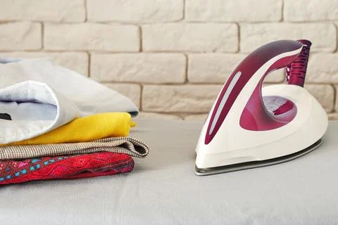 Modern electric iron and stack of folded clothes on the board Stock Photos
