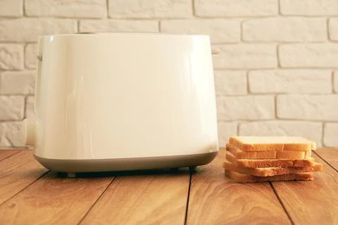 Modern electric toaster and a stack of fresh bread slices on the wooden table Stock Photos
