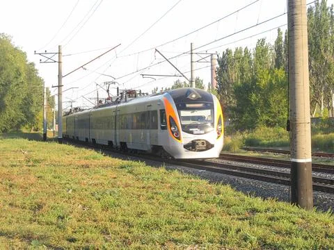 A modern electric train, streamlined in white, blue, and orange, is depicted  Stock Photos